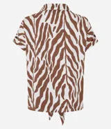 Blusa de manga corta confeccionada en viscosa, con cuello camisero, cierre frontal con botones y detalle de lazo para anudar en el bajo. Presenta un estampado híbrido entre follaje y animal print de cebra en tonos marrón y blanco.