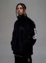 Campera de textura afelpada en color negro, con cuello alto y cierre frontal. Presenta letras bordadas en color blanco en la espalda y en las mangas. Cuenta con ajuste en la cintura y un corte regular.