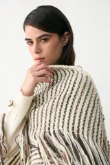 Poncho triangular tejido con diseño de rayas verticales en tonos crudo, marrón y negro, con detalle de hilo de lurex brillante y terminación de flecos largos en todo el borde.