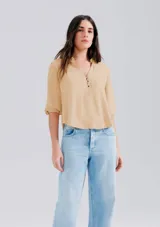 Blusa color marrón claro, con cuello mao y escote en V, manga 7/8 con puños elásticos y cierre frontal parcial con botones.