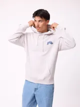 Canguro con capucha y cordones ajustables, de color gris claro. Presenta un logo bordado en el pecho y un parche decorativo en el puño de la manga derecha. Cuenta con un bolsillo frontal tipo canguro y puños acanalados.