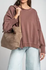 Cartera tipo shopper de gamuza sintética color marrón, con diseño estructurado, asa de hombro ajustable y detalle de placa metálica dorada con logo en la parte frontal.