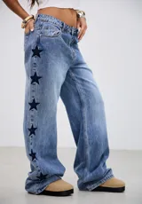 Jean de tiro medio con corte recto y holgado, confeccionado en denim azul. Presenta un diseño con estrellas bordadas en color oscuro a lo largo de las costuras laterales.