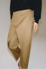 Pantalón de tiro medio confeccionado en mezcla de lyocell, con diseño de pliegues delanteros superpuestos y bolsillos laterales ocultos en costura.
