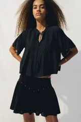 Pollera corta negra con cintura en V decorada con ojales metálicos. Presenta pliegues en la parte superior y un frunce que da volumen a la falda.