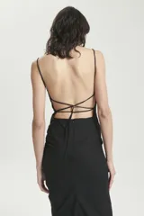 Vestido midi negro de breteles finos, confeccionado en gabardina liviana elastizada. Tiene calce entallado, recortes en el delantero, cierre invisible en la espalda y drapeado lateral en la falda. La espalda es descubierta con tiras cruzadas que se atan en la cintura.