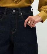 Pantalón de jean corte carrot, color azul oscuro, con cintura alta, cierre frontal con cremallera y botón, y bolsillos laterales.