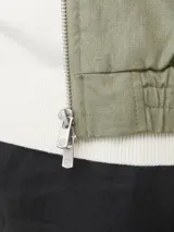 Campera bomber color verde claro, de tejido liviano de lino y algodón, con cuello tipo baseball, mangas largas con puños de canalé, cierre con cremallera y bolsillos delanteros.