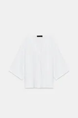Top fluido de punto liso en color blanco, con escote en V pronunciado y mangas cortas amplias.