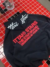 Hoodie negro de corte oversize con capucha, confeccionado en algodón. Presenta un estampado gráfico en color rojo en la espalda con la leyenda 'ITTAI STARS THE STAR BRAND DESIGNED IN VENICE' y un detalle bordado en blanco en la parte posterior de la capucha.