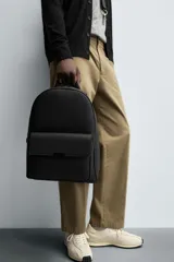 Mochila negra con acabado grabado, compartimento principal con cierre de cremallera, bolsillo interior con cremallera, bolsillo frontal con solapa y cremallera, parte posterior acolchada con banda de sujeción para equipaje, asa de mano y dos asas de hombro ajustables.