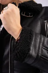 Campera tipo gamulán de cuero sintético marrón oscuro con interior y detalles de corderito sintético en cuello y puños. Presenta cierre frontal, bolsillos laterales con cierre y correas ajustables en el cuello.