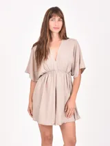 Monoprenda corta color beige, con escote en V profundo, mangas cortas tipo mariposa y cintura fruncida con elástico.