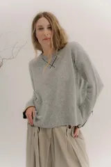 Buzo de lambswool color beige, con escote redondo y detalle en V. Presenta cierres metálicos en los puños que revelan un interior en contraste de color marrón y ribete rojo. Tiene tajos laterales para mayor comodidad y un fit amplio.