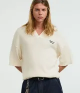 Camisa polo de hombre confeccionada en tejido de punto de algodón, color crema, con cuello en V y manga corta. Presenta un corte oversized y un pequeño bordado de lettering en el pecho.