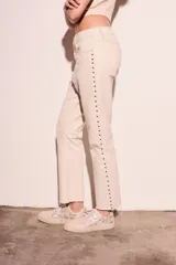 Pantalón de jean color crudo, corte flare, tiro medio y detalle de tachas plateadas en los laterales.