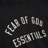 Camiseta negra de algodón con cuello redondo y corte ultra oversize. Estampado frontal con el texto "FEAR OF GOD ESSENTIALS" en color crema.