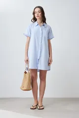 Vestido camisero corto color celeste melange, con cuello camisero y volados en el cuello, la tapeta de botones y los puños de las mangas cortas. Tiene un bolsillo de parche en el pecho.