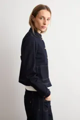 Chaqueta de jean azul oscuro, con cuello mao, cierre frontal de botones metálicos y dos bolsillos frontales de parche.