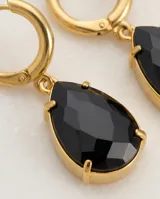 Caravanas colgantes de acero con baño de oro, compuestas por una argolla pequeña y un dije en forma de gota con piedra negra.