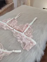 Conjunto de lencería compuesto por un bralette triangular y una bombacha tipo tanga, confeccionados en encaje floral color coral con detalles de elásticos en tono champagne.