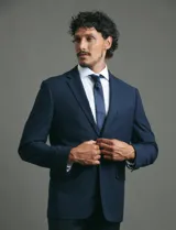 Saco de vestir azul marino con cuello solapa, manga larga y cierre frontal de dos botones. Presenta un diseño clásico con bolsillos laterales con solapa y un bolsillo superior en el pecho.