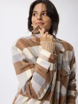 Sobrecamisa de corte holgado con estampado de cuadros en tonos beige, marrón y gris. Presenta cuello clásico, cierre frontal con botones, bolsillos delanteros con solapa y puños tejidos acanalados. El interior está forrado con tejido tipo sherpa para mayor calidez.