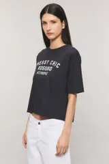 Remera Kosiuko de algodón color blanco, de corte regular y mangas cortas hasta el codo. Cuenta con un diseño estampado en el frente con la leyenda "Messy Chic Kosiuko St. Tropez".