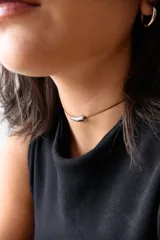 Gargantilla minimalista compuesta por un hilo encerado fino y un dije central de acero quirúrgico en forma de tubo curvo.