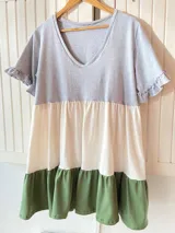 Vestido corto de corte evasé con paneles de color gris en la parte superior, blanco en el centro y verde en el ruedo. Tiene mangas cortas con volados.