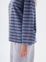 Remera de manga larga con calce holgado, confeccionada en algodón. Presenta un diseño a rayas horizontales en tonos beige y negro, con bordado de letras SP en el pecho y estampa de la marca en la manga.