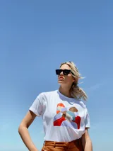 Remera blanca de corte oversized con estampado de figuras femeninas abstractas en colores rojo, marrón, celeste y lila.