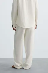 Pantalón de corte relajado confeccionado en tejido de cáñamo color blanco roto. Presenta cintura elástica con cordón interior ajustable, cierre frontal con botones, bolsillos laterales y un bolsillo trasero de plastrón.