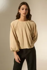 Blusa de color beige con cuello redondo y mangas largas abullonadas con puños elásticos. Presenta un corte holgado y fluido.
