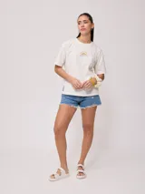 Remera color salmón de corte holgado, con estampado pequeño en el frente que incluye un arcoíris y el texto "Rusty Club".