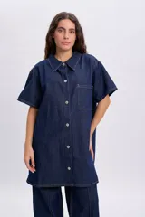 Vestido corto de jean azul oscuro, de manga corta, con cuello camisero, cierre frontal de botones metálicos y un bolsillo aplicado en el pecho.