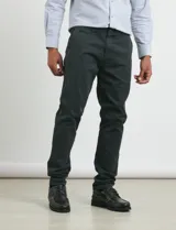 Pantalón de vestir verde oliva, de corte slim fit, sin pinzas, con bolsillos laterales y traseros. Se ajusta a la cintura con cinturón de cuero marrón.