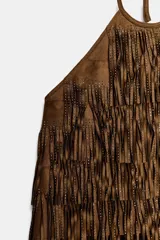 Top de cuello halter con lazada, confeccionado en tejido efecto ante. Presenta un diseño cubierto de flecos con tachas aplicadas en toda la superficie.