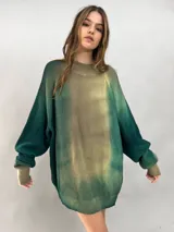 Buzo tejido de lana merino con diseño oversize, manga ranglan y cuello levemente elevado. Presenta un efecto de teñido degradado que combina tonos verdes y beige.
