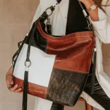 Cartera tipo hobo de cuero vacuno con diseño de bloques de color blanco, marrón y negro. Tiene correa de mano corta y correa bandolera larga ajustable.