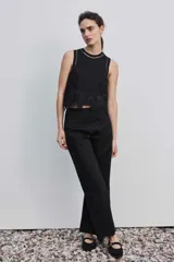 Blusa negra sin mangas de corte cropped, con cuello redondo y detalles de bordados calados y perforados en forma de flores en el borde inferior y en los hombros.