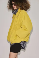 Cazadora bomber de cuello subido ajustable con cordones, manga larga con puños elásticos y cierre frontal con cremallera y botones a presión ocultos bajo solapa. Cuenta con bolsillos delanteros y diseño holgado.