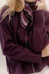 Polera tejida en lambswool color beige, con cuello alto y diseño de intarsia en tonos marrones y grises. Presenta botones forrados en el cuello para modular la apertura.