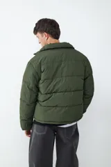 Campera puffer de color verde militar con cuello alto, cierre frontal de cremallera y bolsillos laterales funcionales.