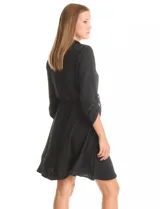Vestido corto negro de crepe, con cuello solapa y escote en V. Presenta bolsillos simulados con cierres metálicos dorados en la parte delantera y mangas largas regulables con presilla y botón. La cintura es elastizada.