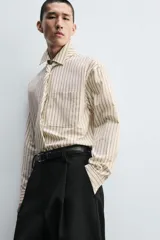 Camisa de corte relajado confeccionada en algodón, con estampado de rayas verticales. Presenta cuello solapa, manga larga con puños abotonados, bolsillo frontal y corbata integrada del mismo tejido.
