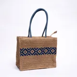 Bolso tipo tote de yute color beige con diseño geométrico azul y asas de soga azul.