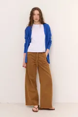 Jean tostado de corte wide leg, tiro medio con presillas y lazo ajustable en la cintura. Presenta bolsillos delanteros y traseros, costuras decorativas verticales y terminación desmechada en el ruedo.