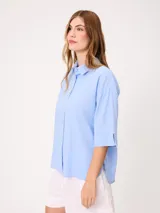 Camisa de manga corta celeste, confeccionada en mezcla de algodón y lino, con cuello camisero y cierre frontal de botones.