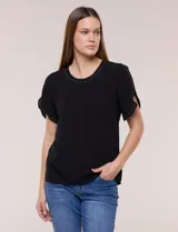 Blusa holgada de color negro, con escote redondo y mangas cortas adornadas con apliques de tachas metálicas. Presenta delicadas tablas centrales en el frente y un diseño elegante.